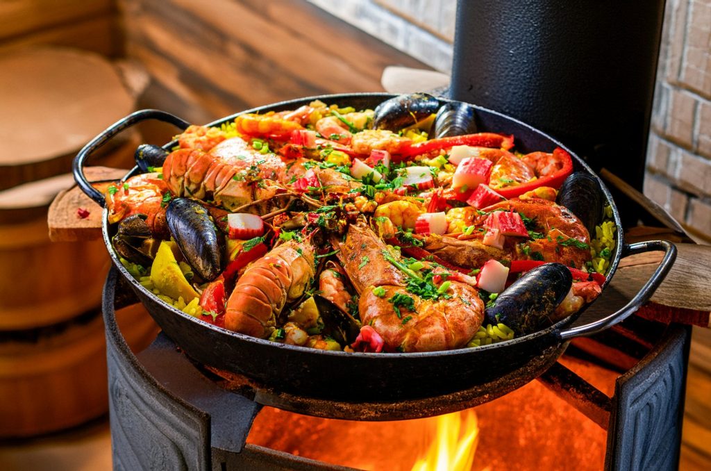 Deliciosa paella de mariscos chisporroteando sobre una llama abierta, rellena de ingredientes coloridos.