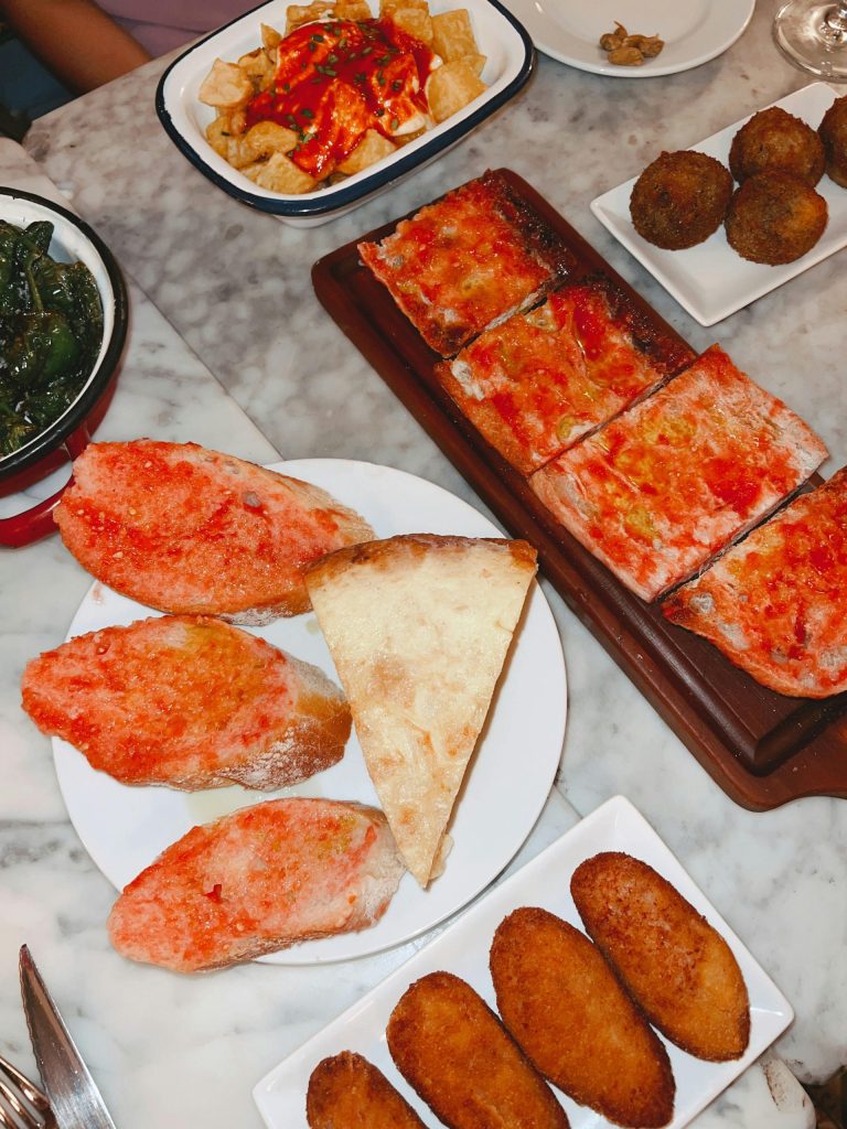 Una vibrante variedad de tapas españolas que incluyen patatas bravas, pan con tomate y croquetas en una mesa de mármol.